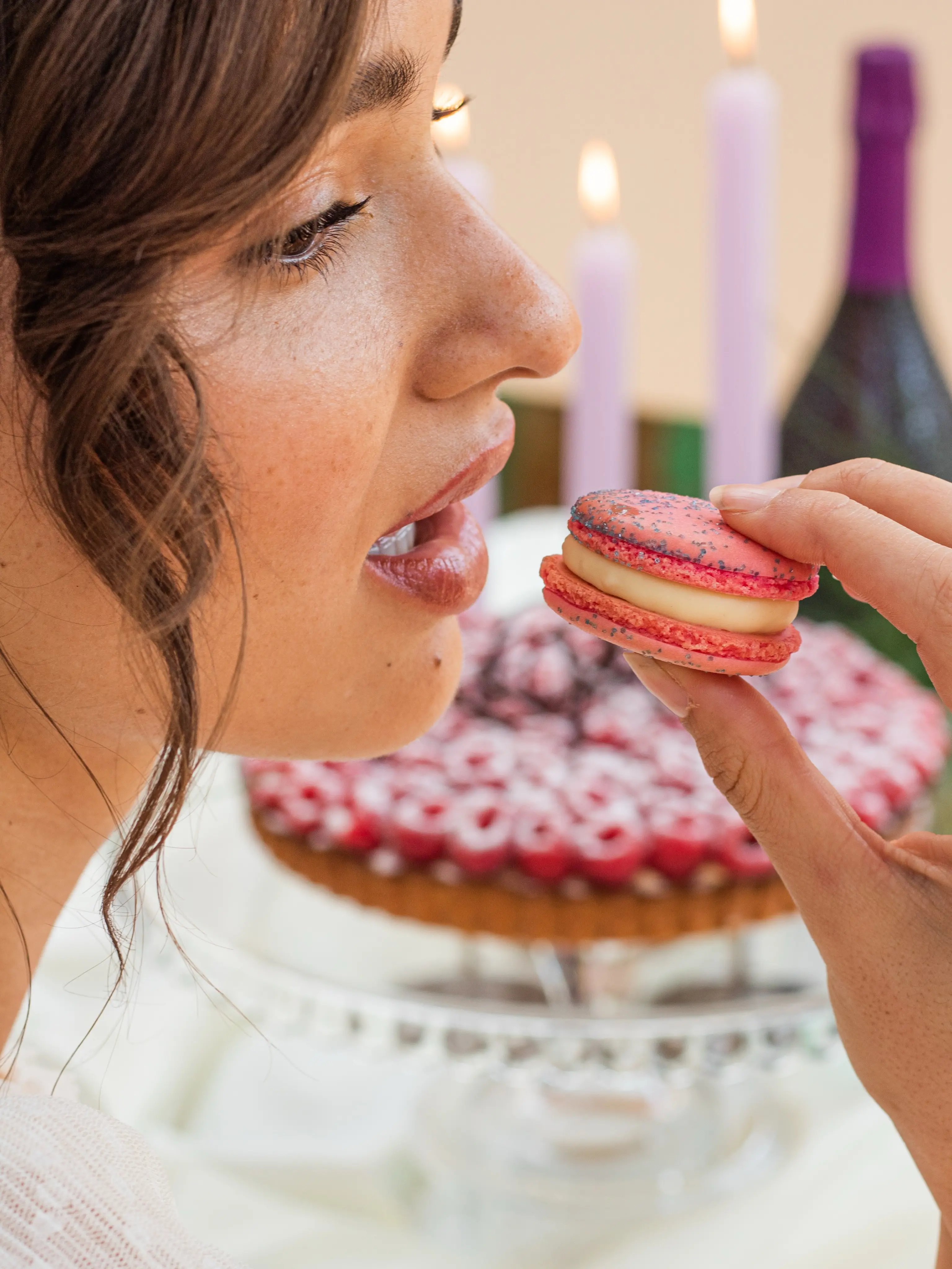 Vrouw neemt een hap van een roze macaron bij een taart met kaarsen