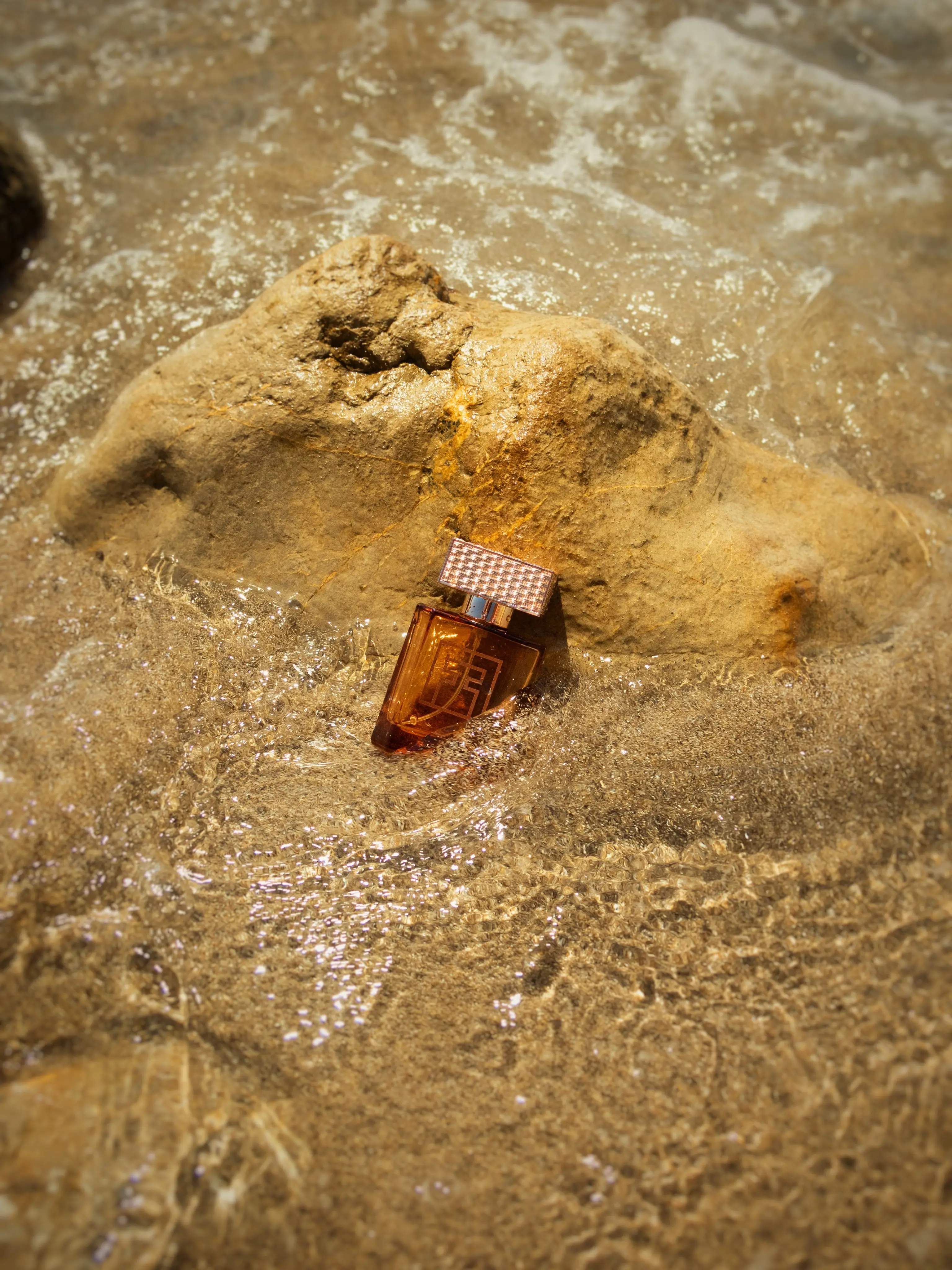 Een flesje parfum tussen de rotsen in ondiep, goudkleurig zeewater op Ibiza