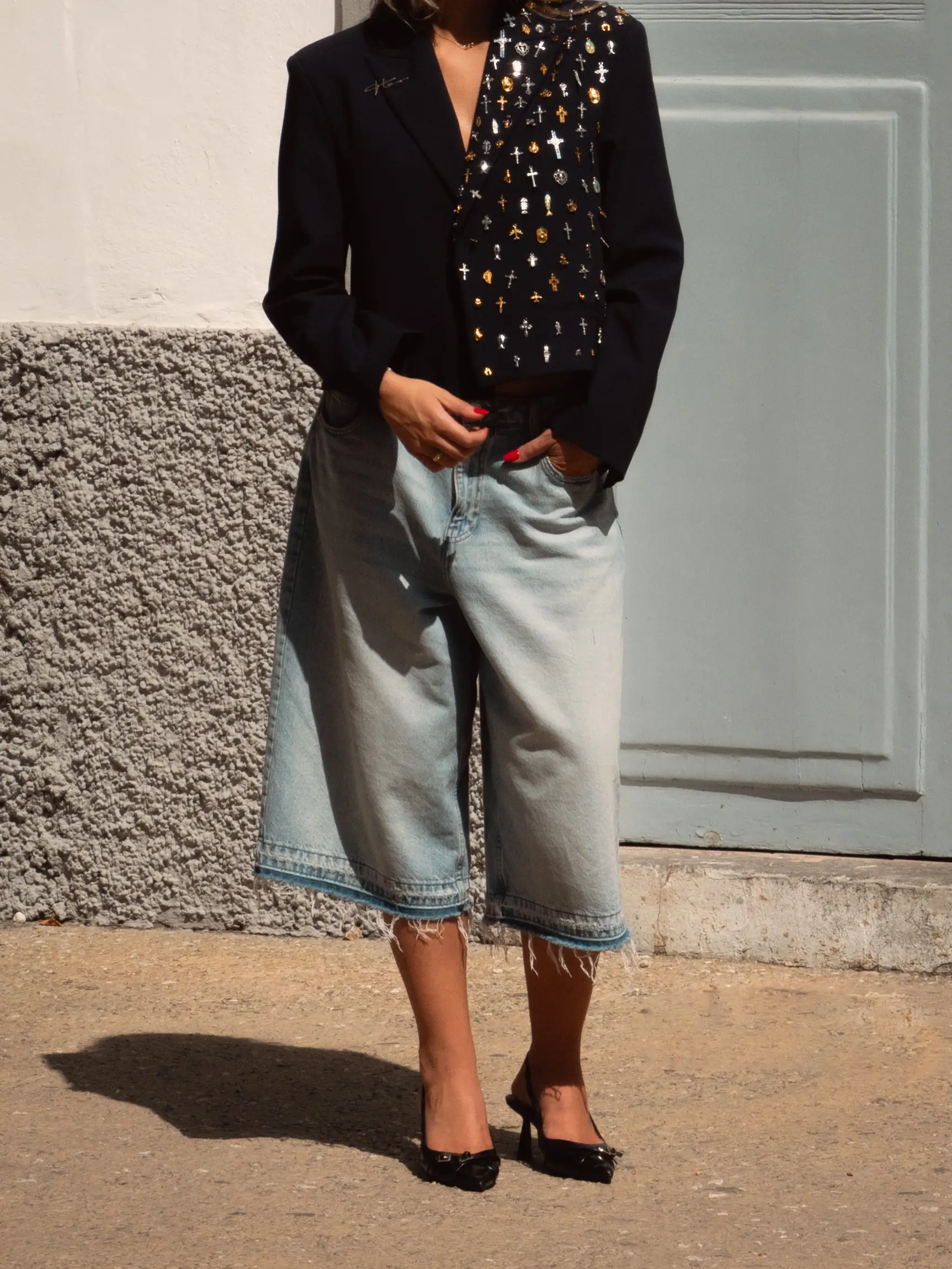 Model in een zwarte blazer met pins en wijde jeans voor een lichte muur op Ibiza