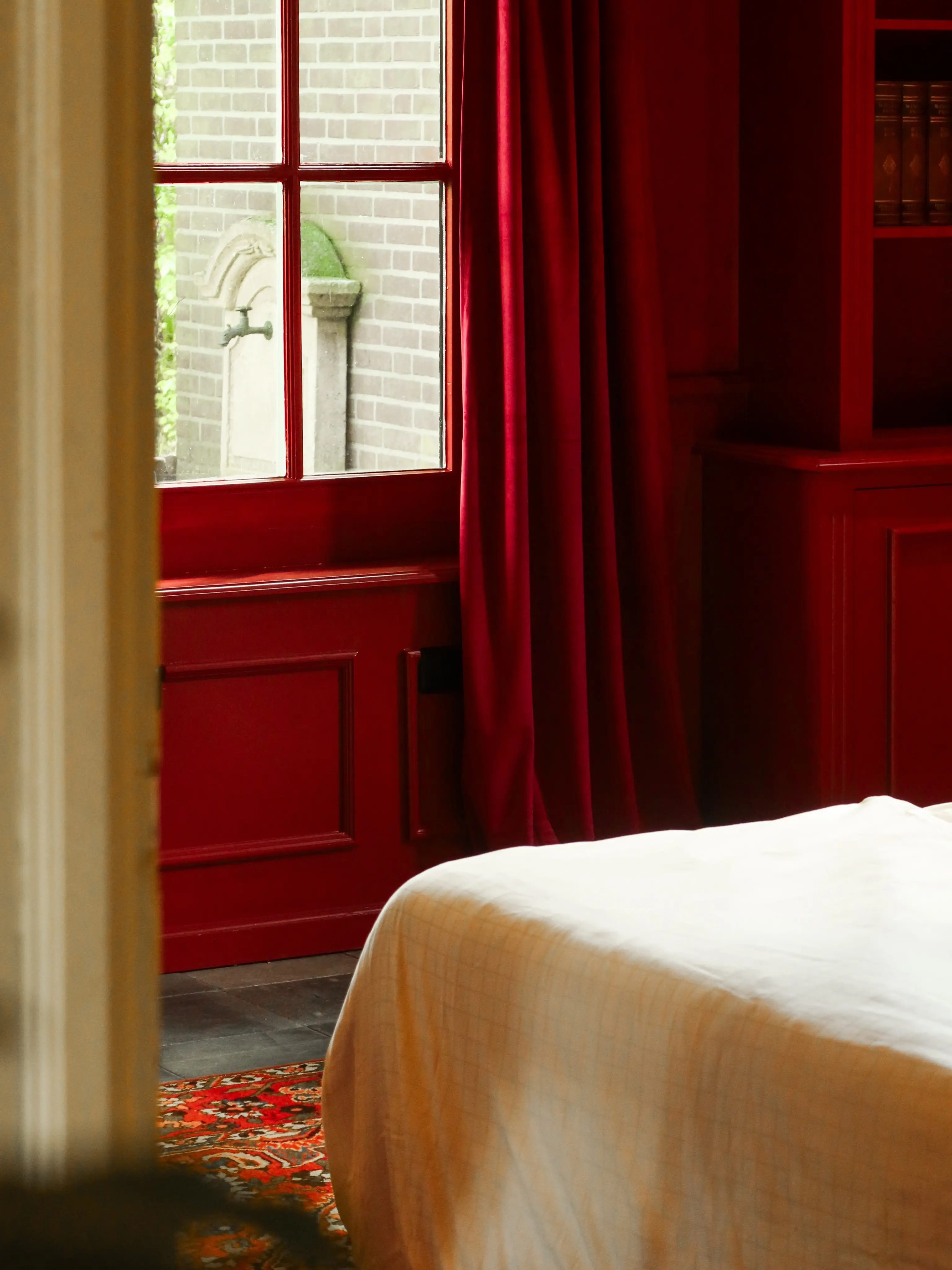 Slaapkamer met rood houtwerk, rood gordijn en een bed met crèmekleurig beddengoed