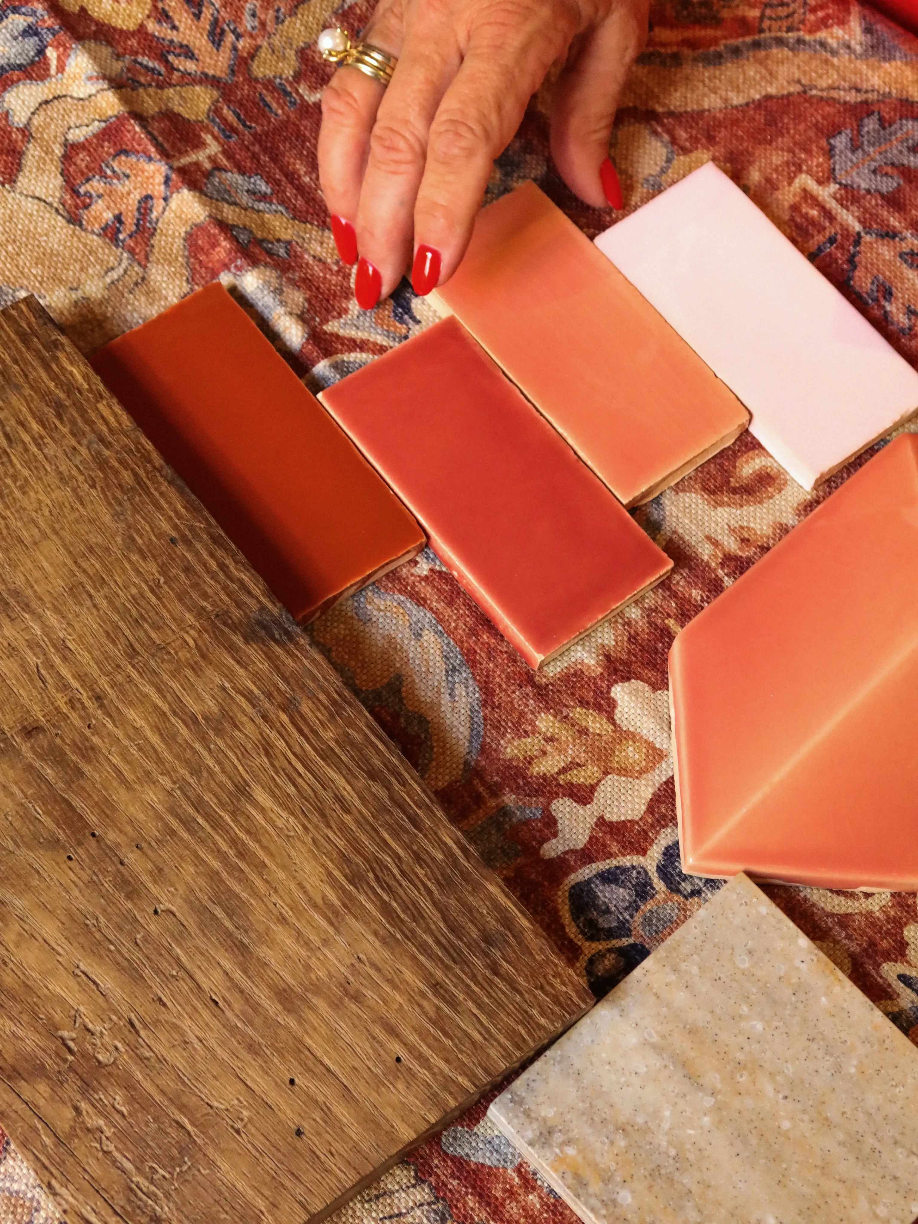 Hand met rode nagels schikt oranje en roze tegels op een gekleurd tapijt
