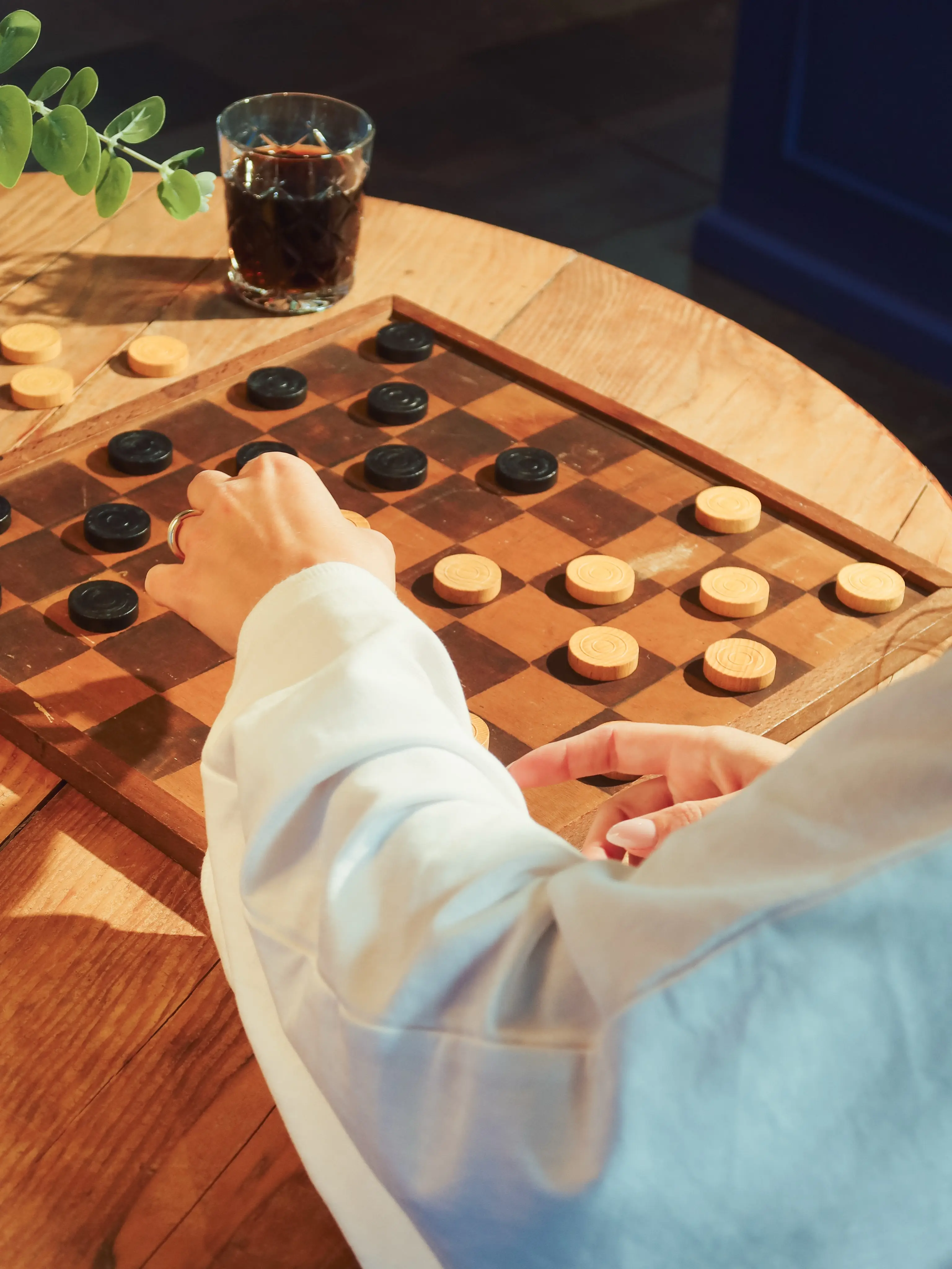 Hand speelt een damspel op een houten tafel, met een glas cola ernaast