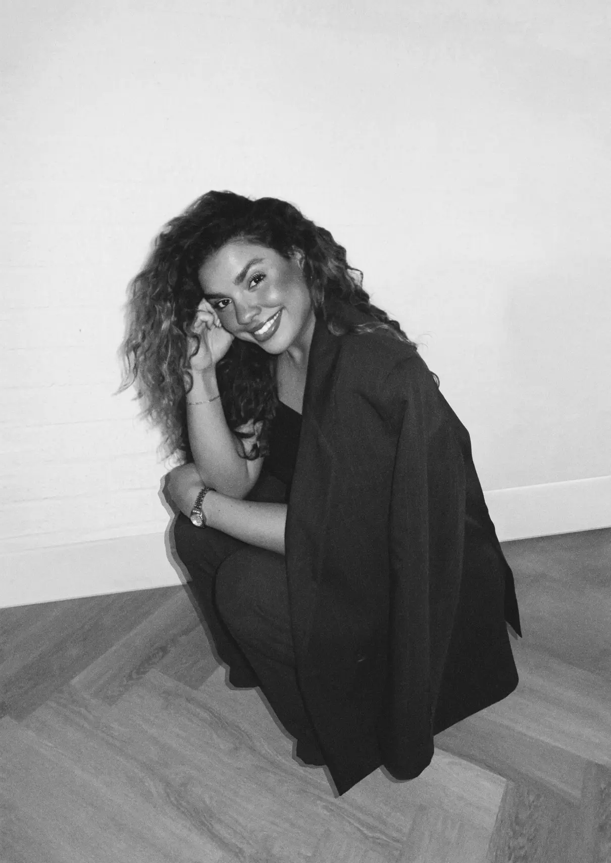 Kelly Bobson, zwart-witportret: lachend, hurkend in een zwarte blazer