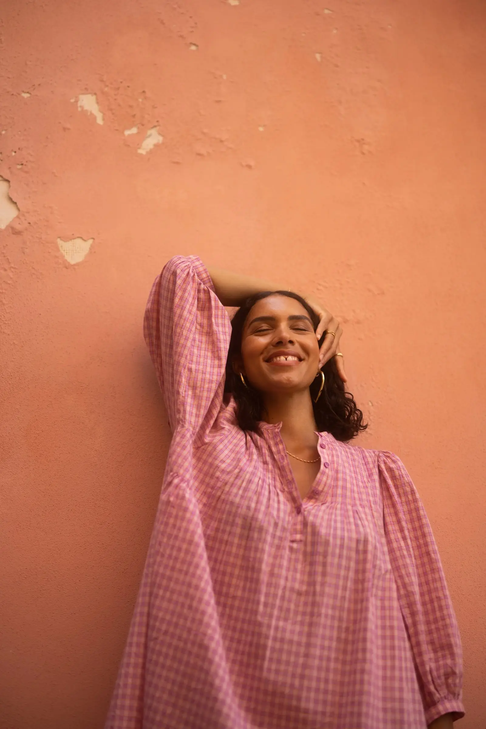 Lachende vrouw in een roze blouse tegen een oranje muur